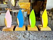 The 4 variations of the 'Happa' Leaf Shaped All - Around Knife by Asano Blacksmith (pink, blue, green and yellow) on each of their respective stands and aligned next to each other in the workshop