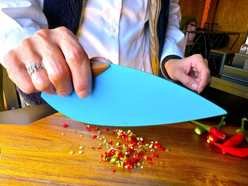 Closeup of hands using the Blue 'Happa' Leaf Shaped All - Around Knife by Asano Blacksmith cutting vegetables over a wooden cutting board inside a kitchen