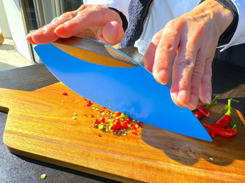 Closeup of hands using the Blue 'Happa' Leaf Shaped All - Around Knife by Asano Blacksmith cutting vegetables over a wooden cutting board