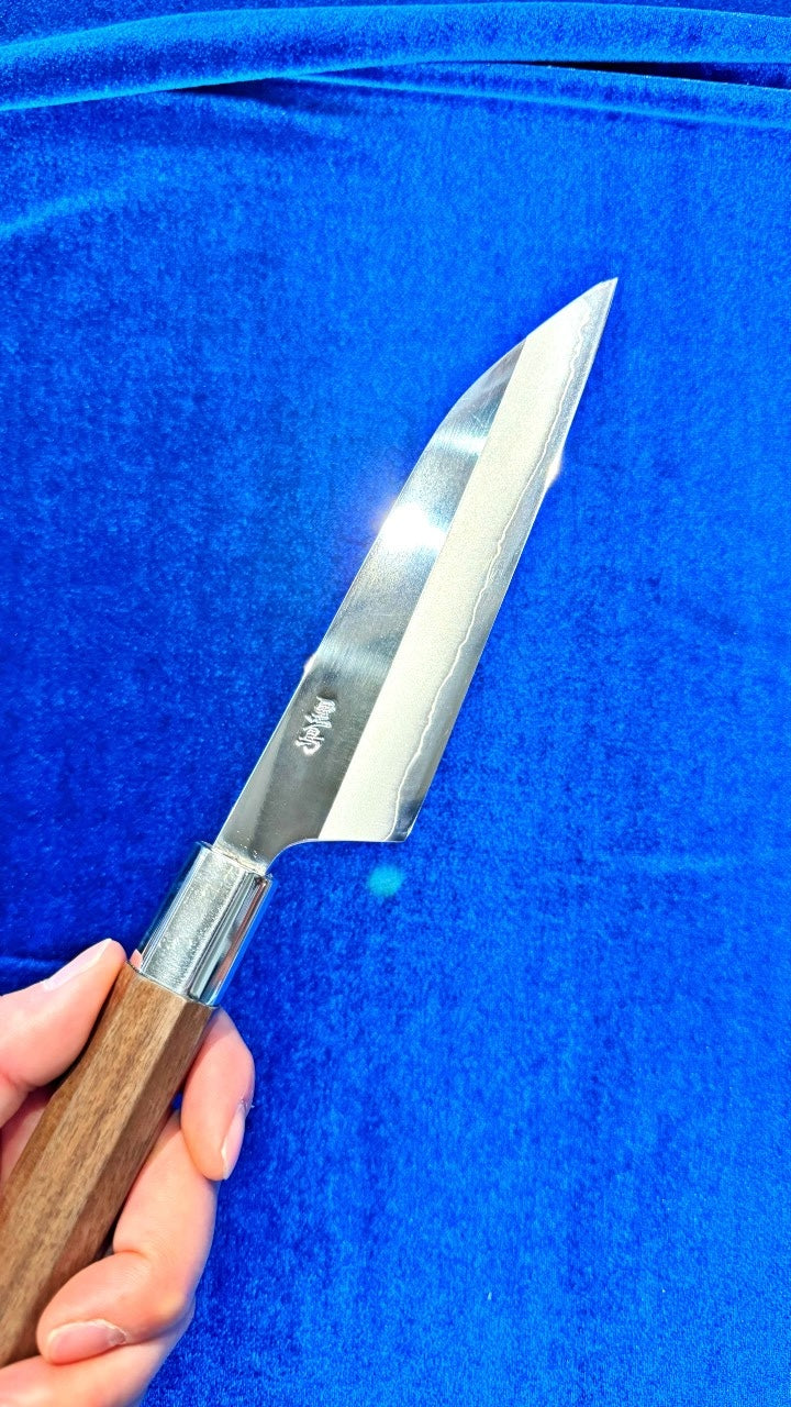 Holding Kurotori Knife Petit Size in one hand, with blue background