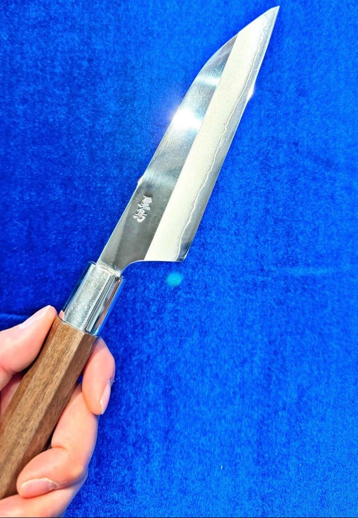 Holding Kurotori Knife Petty Size in one hand, with blue background at an angle