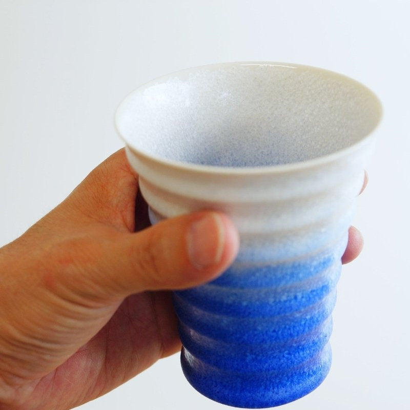 Hand holding indigo-white gradient Ceramic Aritaware Cup by Imari Togei craftsmen on white background