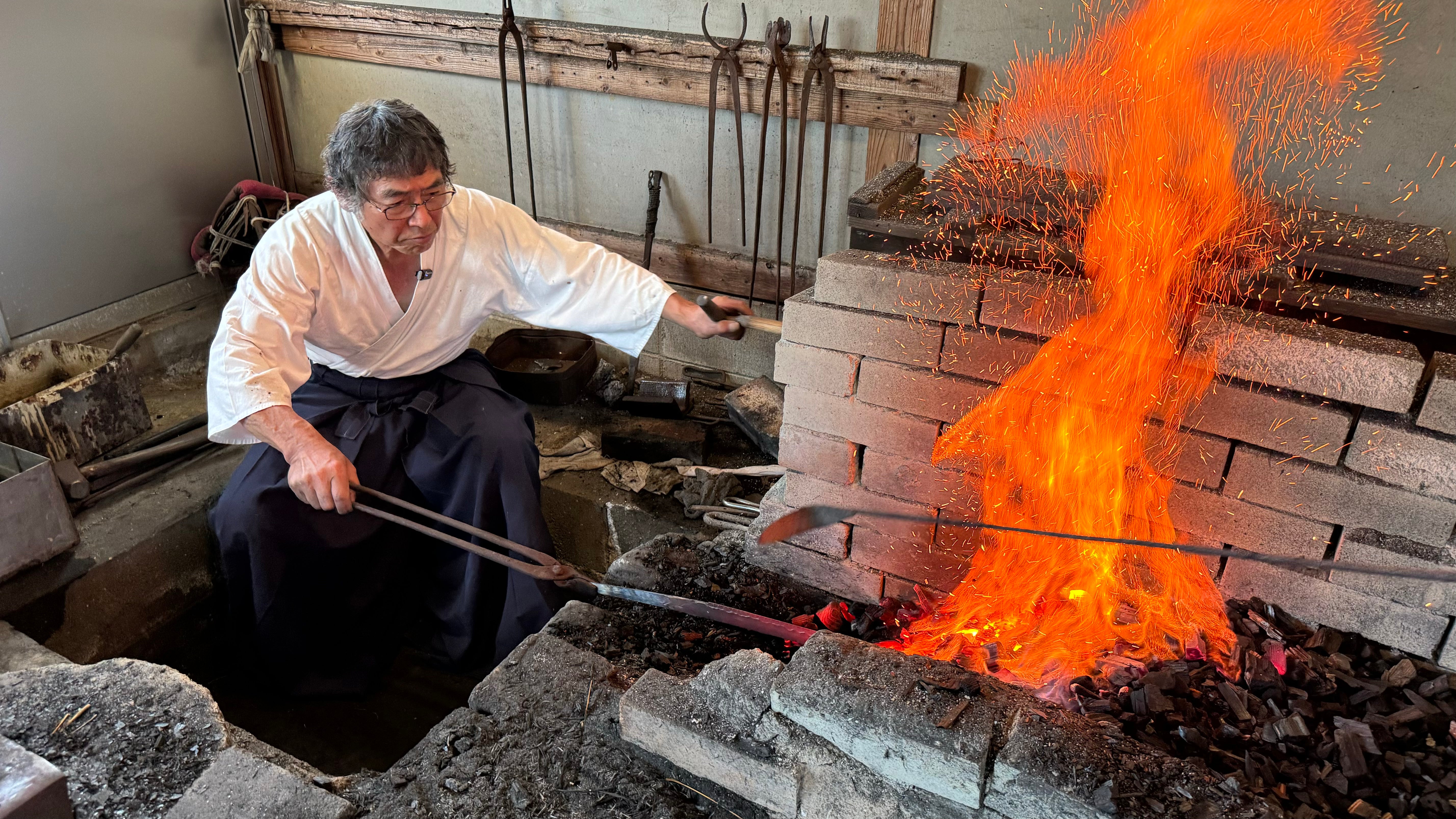 Shirou Kunimitsu master blacksmith in hakama clothes heating a blade while sparks fly