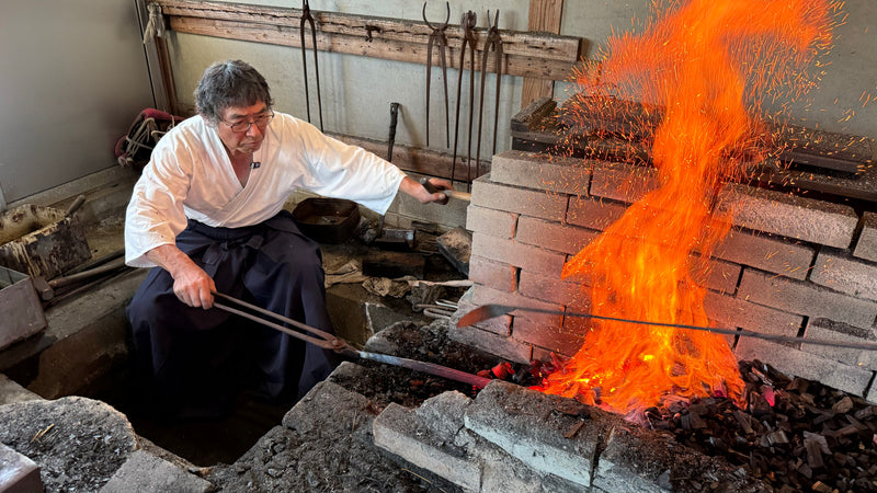 Shirou Kunimitsu master blacksmith in hakama clothes heating a blade while sparks fly