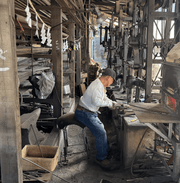 Nakamura Blacksmith master craftsman, Toshio Nakamura, inside the workshop full o machines and metal pieces examining a blade