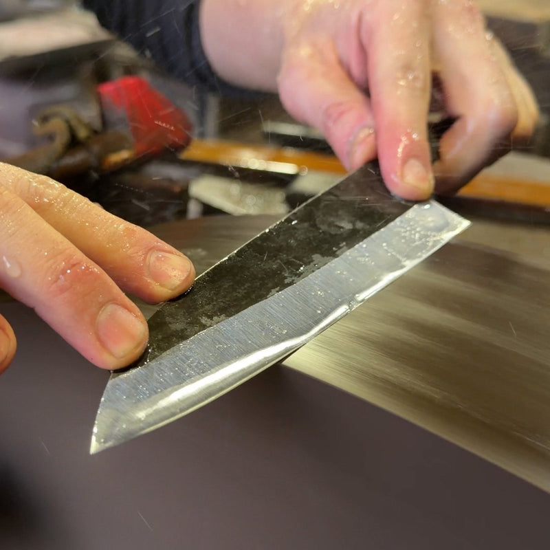 Closeup of hands sharpening a gyuto blade in the Sakoda Hamono workshop