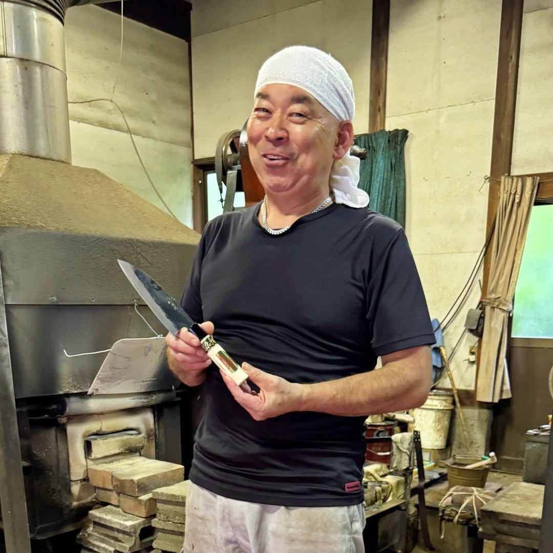 Shigemitsu Hamono craftsman  smiling while holding one of his knives in the workshop