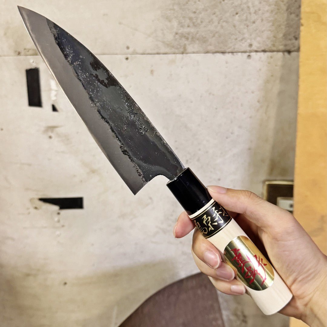 Hand holding Thin Kurouchi Deba Knife 155mm by Shigemitsu Hamono in workshop