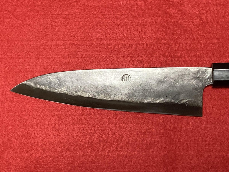 Closeup on blade of Kurouchi Gyuto Kitchen Knife 180mm crafted by Kawasaki Blacksmith on red background (front)