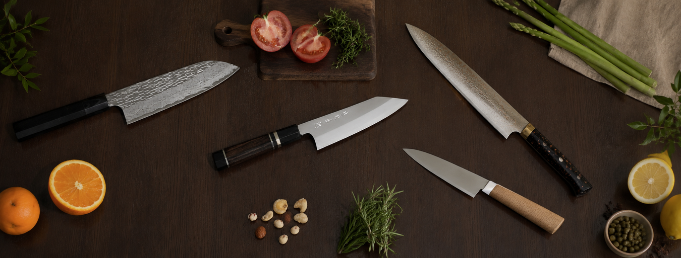 Above perspective of a Nigara Hamono Santoku knife, a Tadokoro Hamono Omoi Ginsan Kiritsuke knife, a KISEKI santoku knife and a Takeshi Saji Gyuto knife over a kitchen table