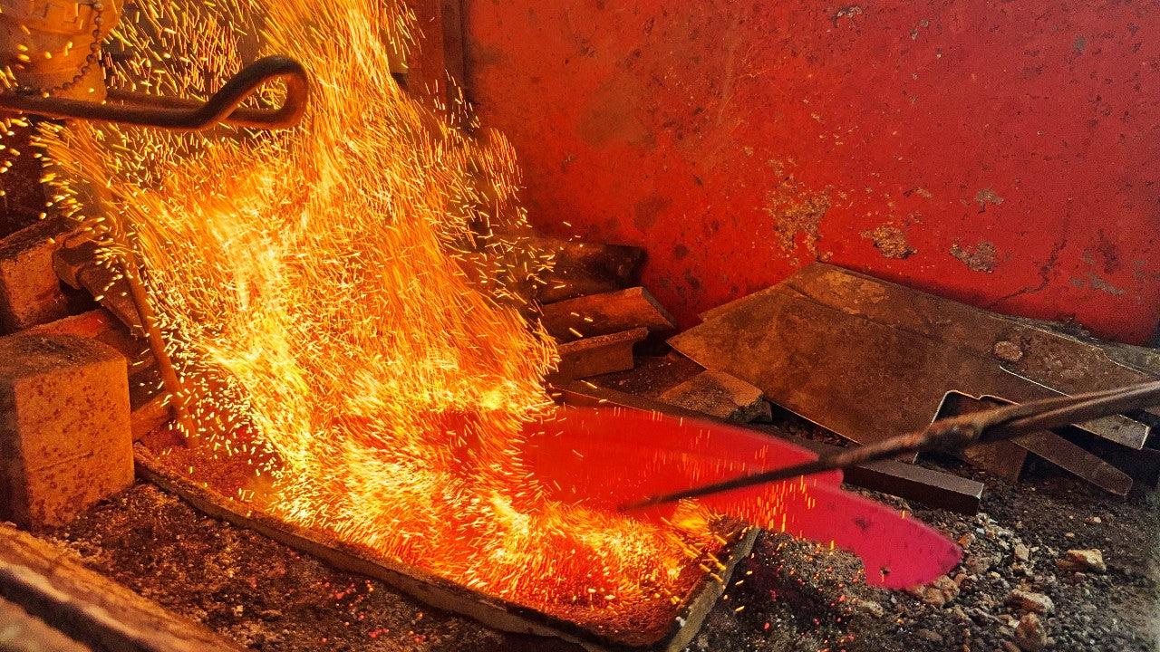 Knife is being crafted by heating it in a forge, fire sparks flying around