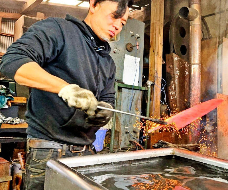 Artisan in the Kurotori Blacksmith workshop holding a heated blade before a water tank for cooling