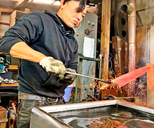 Artisan in the Kurotori Blacksmith workshop holding a heated blade before a water tank for cooling