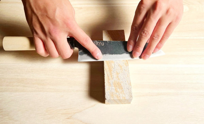 Closeup of the Minomo Blacksmith Santoku Knife being sharpened with the Amakusa Red Sharpening Stone