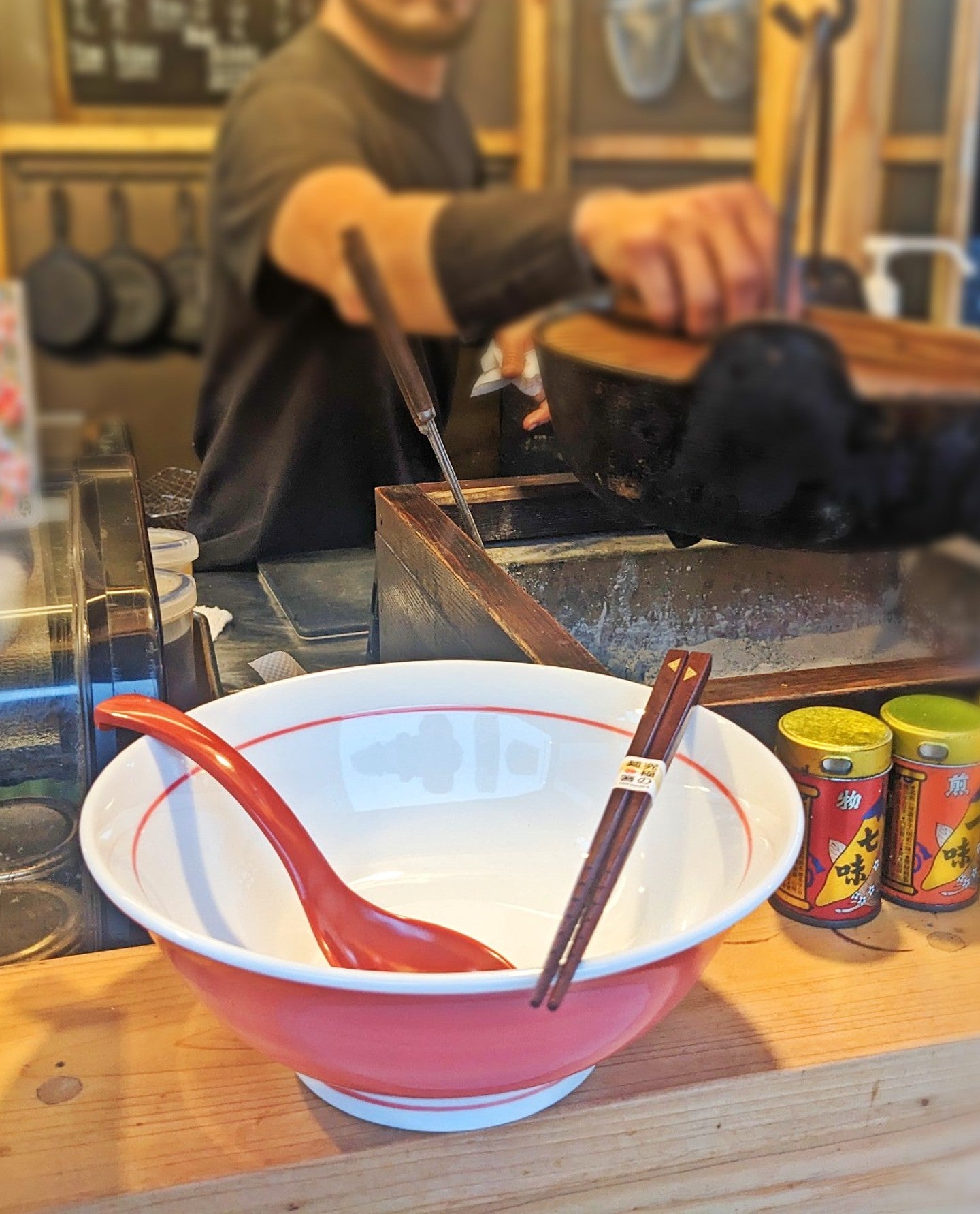 A ramen bowl, chopsticks, and a spoon are placed on the edge of the counter.
