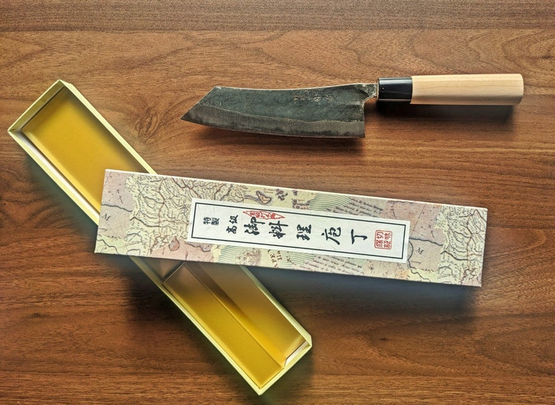 Curved Back Bunka Kitchen Knife 165mm by Nakamura Hamono nexts to its open box showcasing the label with Japanese characters