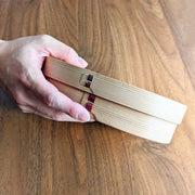 Hand holding Oval Bento Box crafted by Hakata Bentwood Tamaki on wooden background