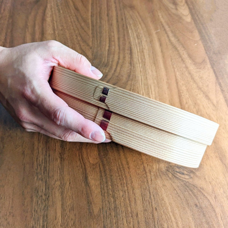 Hand holding Oval Bento Box crafted by Hakata Bentwood Tamaki on wooden background