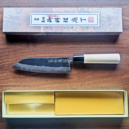 Kurouchi Santoku Knife 165mm by Nakamura Hamono next to its open box showcasing the Japanese label on the cover
