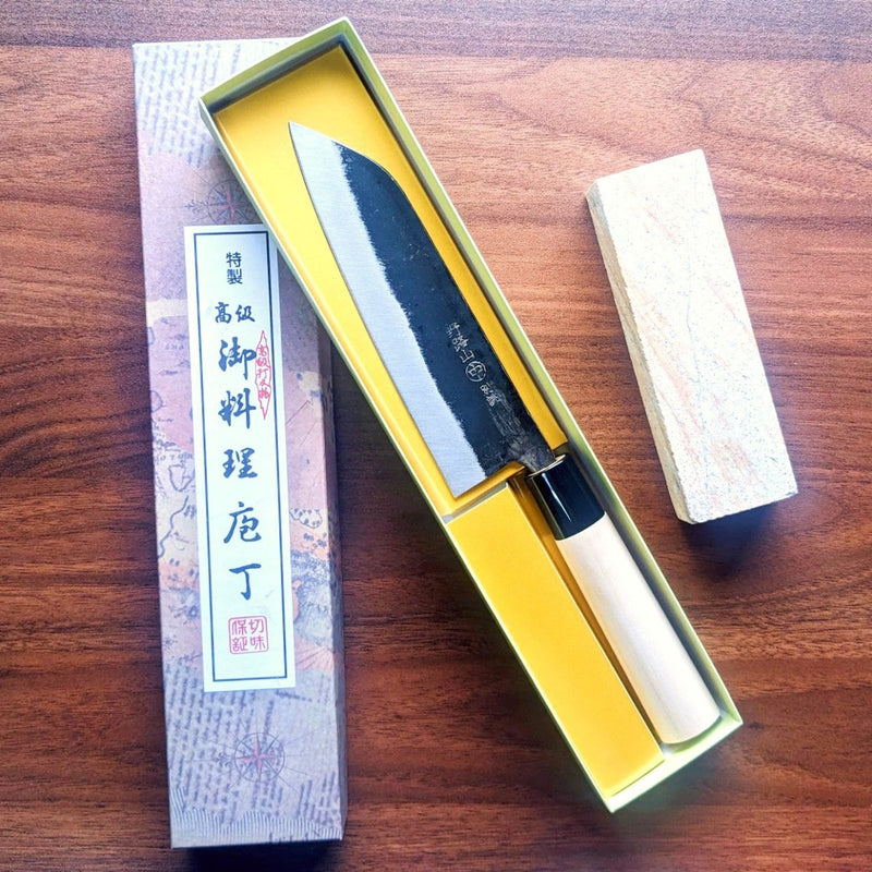 Open box with Japanese label on the cover with the Nakamura Hamono Kurouchi Santoku Knife 165mm inside and the Amakusa Red Sharpening Stone