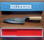 Nakamura Hamono Kurouchi Deba Knife 21cm next to the open box showcasing cover with Japanese label