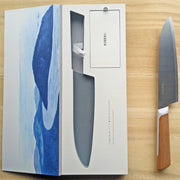 KISEKI Santoku Knife next to its open box over a light wooden background