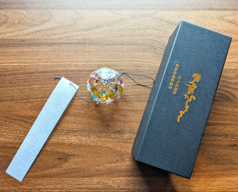 木製の背景に副島ガラス製品による手作りのレインボー風鈴、白い紙が吊り下げられ、左側に黒いボックスが付いています