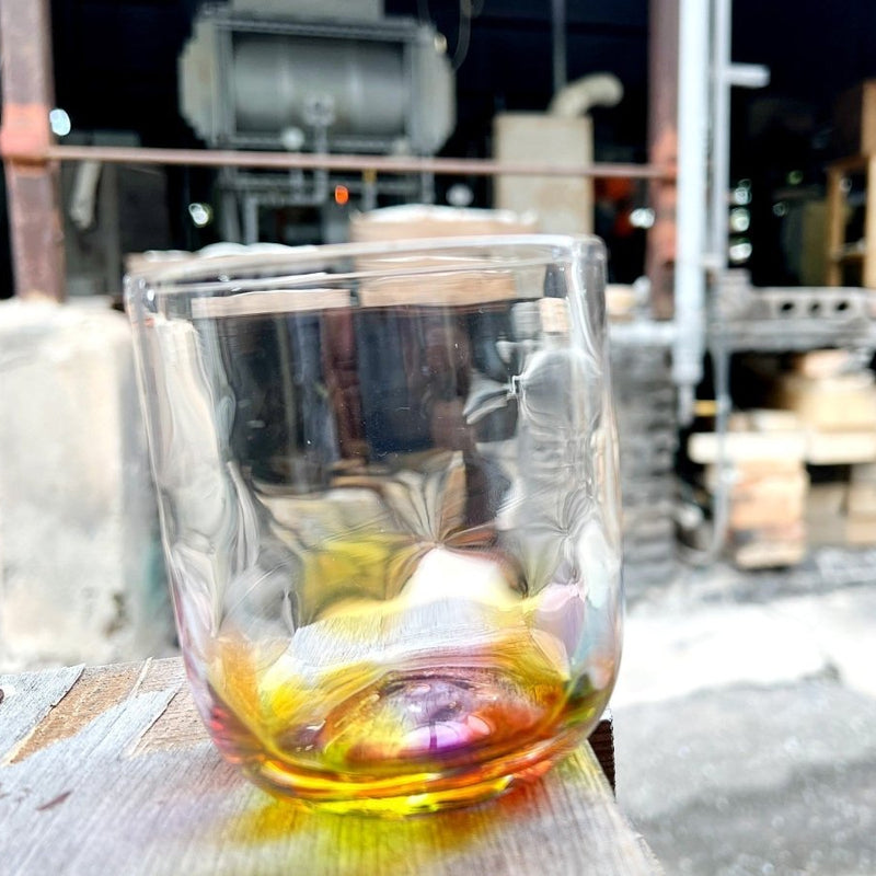 背景にワークショップを備えた木製のテーブルの上にある副島ガラス製品による手作りのレインボーロックグラスのクローズアップ
