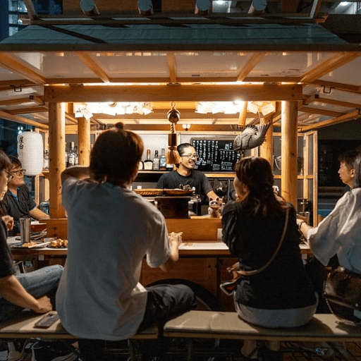 Customers seated in the Yatai Keiji stall eating and talking among them and with Abe-san, the chef