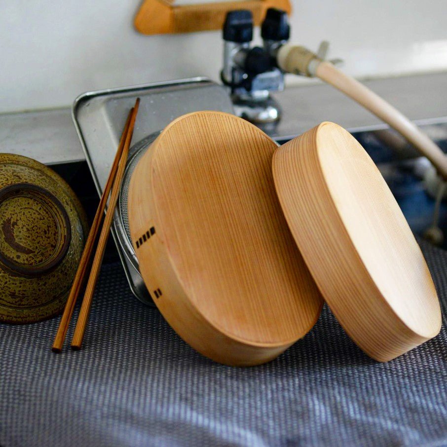 Oval Bento Box crafted by Hakata Bentwood Tamaki with lid drying on blue dish towel with chopsticks and pan