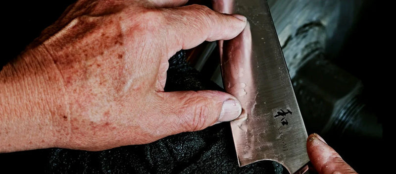 Closeup of a NAGOMI knife balde being polished with the hands holding it showing