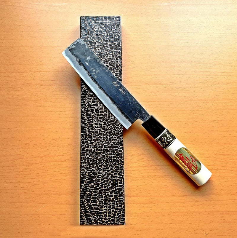 Kurouchi Nakiri Knife 155mm crafted by Shigemitsu Hamono diagonal atop snakeskin box on wood background