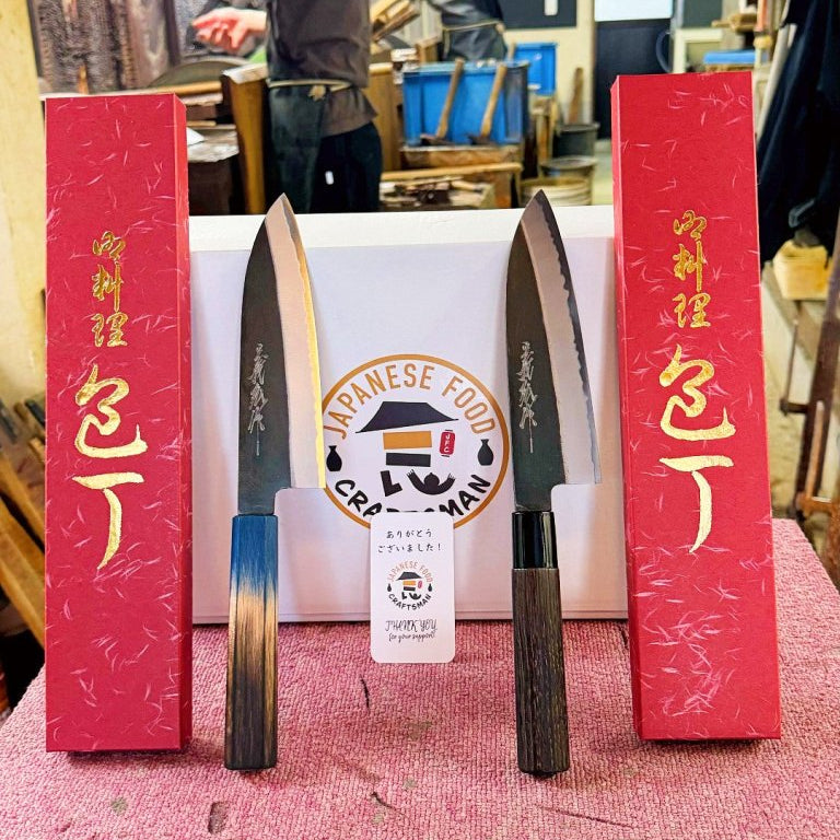 Two Yamawaki Hamono Kurouchi Santoku Knives 180mm on red table leaning on white box