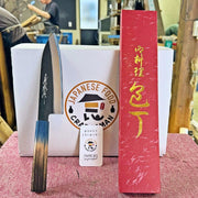 Kurouchi Santoku Knife 180mm by Yamawaki Hamono with blue/brown 
handleon red table leaning on white box with red box