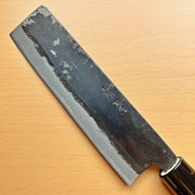 Closeup on blade of Kurouchi Nakiri Knife 155mm crafted by Shigemitsu Hamono diagonal on wood background