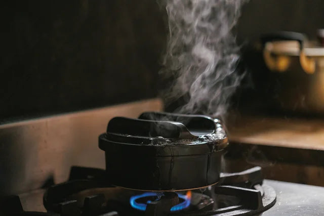 A black pot is simmering and the steam is rising up.
