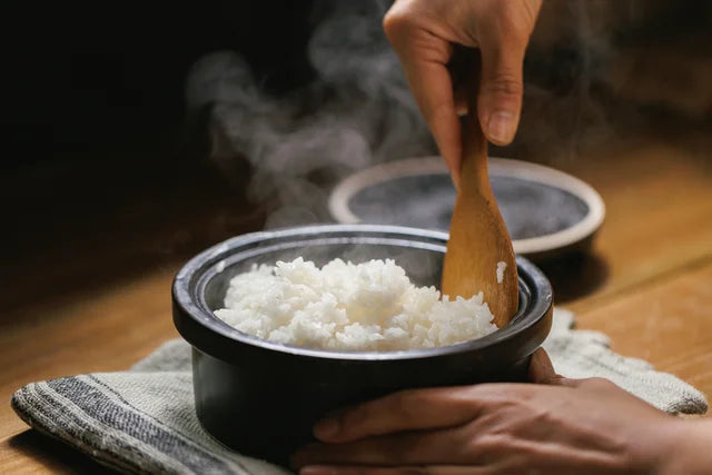 White rice in a pot is being mixed with a wooden rice scoop.