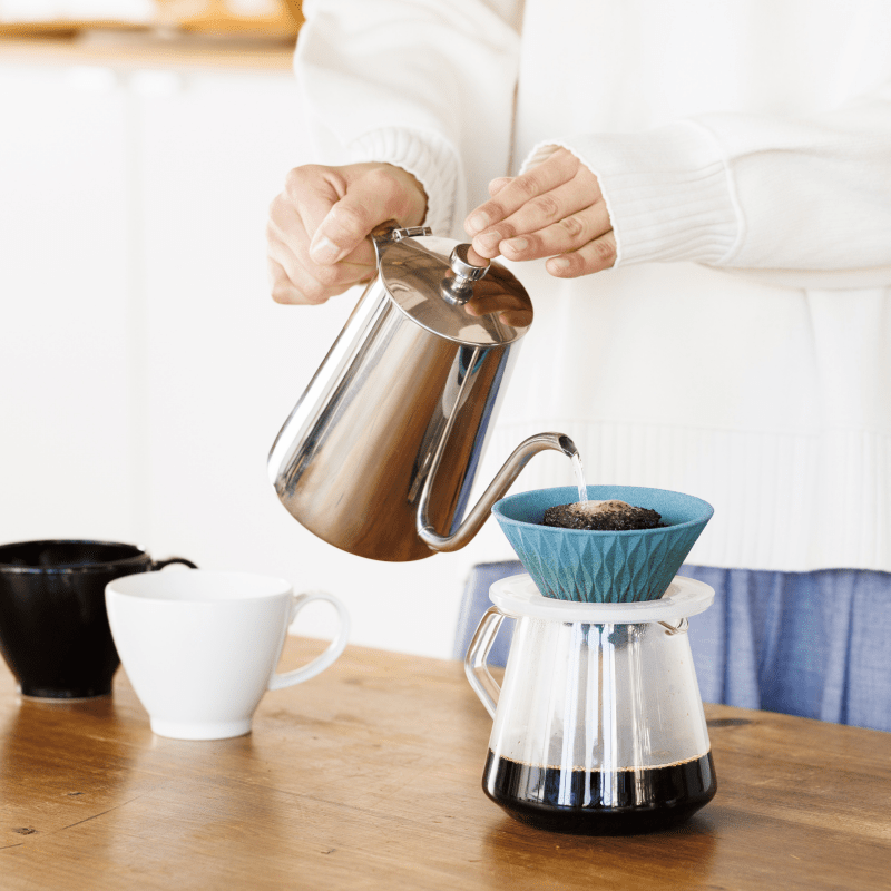 Woman pouring hot water over coffee grinds in blue COFIL Flow Ceramic Coffee Filter over coffee pot