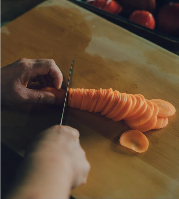 Closeup of a hand holding a KISEKI santoku knife cutting a carrot