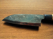 Closeup on blade of Kawasaki Blacksmith Kurouchi Santoku Knife 160mm on wooden background (front)