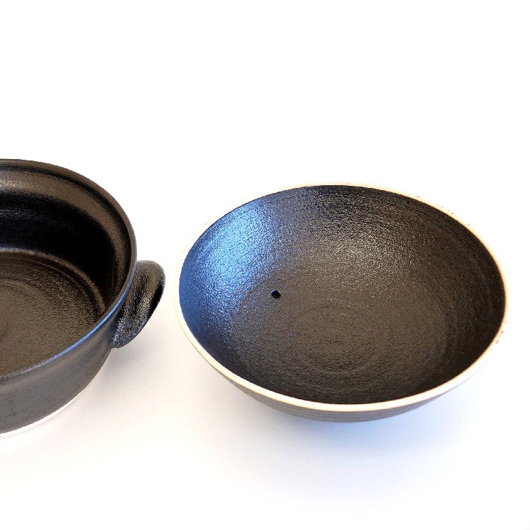 A black lid of pot is placed next to a black clay pot.