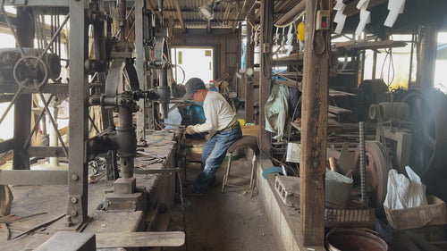 Nakamura Blacksmith's Toshio Nakamura master artisan inside his machine and metal pieces workshop hammering a knife blade