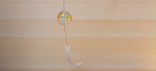 Handcrafted Rainbow Wind Chime by Soejima Glassware hanging vertically in front of light wooden background blowing in the wind