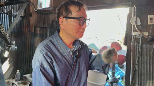 Master swordsmith Ueda Sukesada inside Bizen Osafune workshop taking a hot blade from the forge to hammer it while sparks fly.