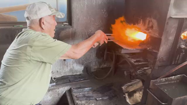 The Grandfather of the MInomo Blacksmith family hammering a blade
