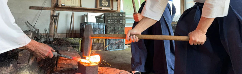 Closeup of the lower body of three Shiro Kunimitsu artisans in traditional hakama clothes hammering by hand a piece of metal